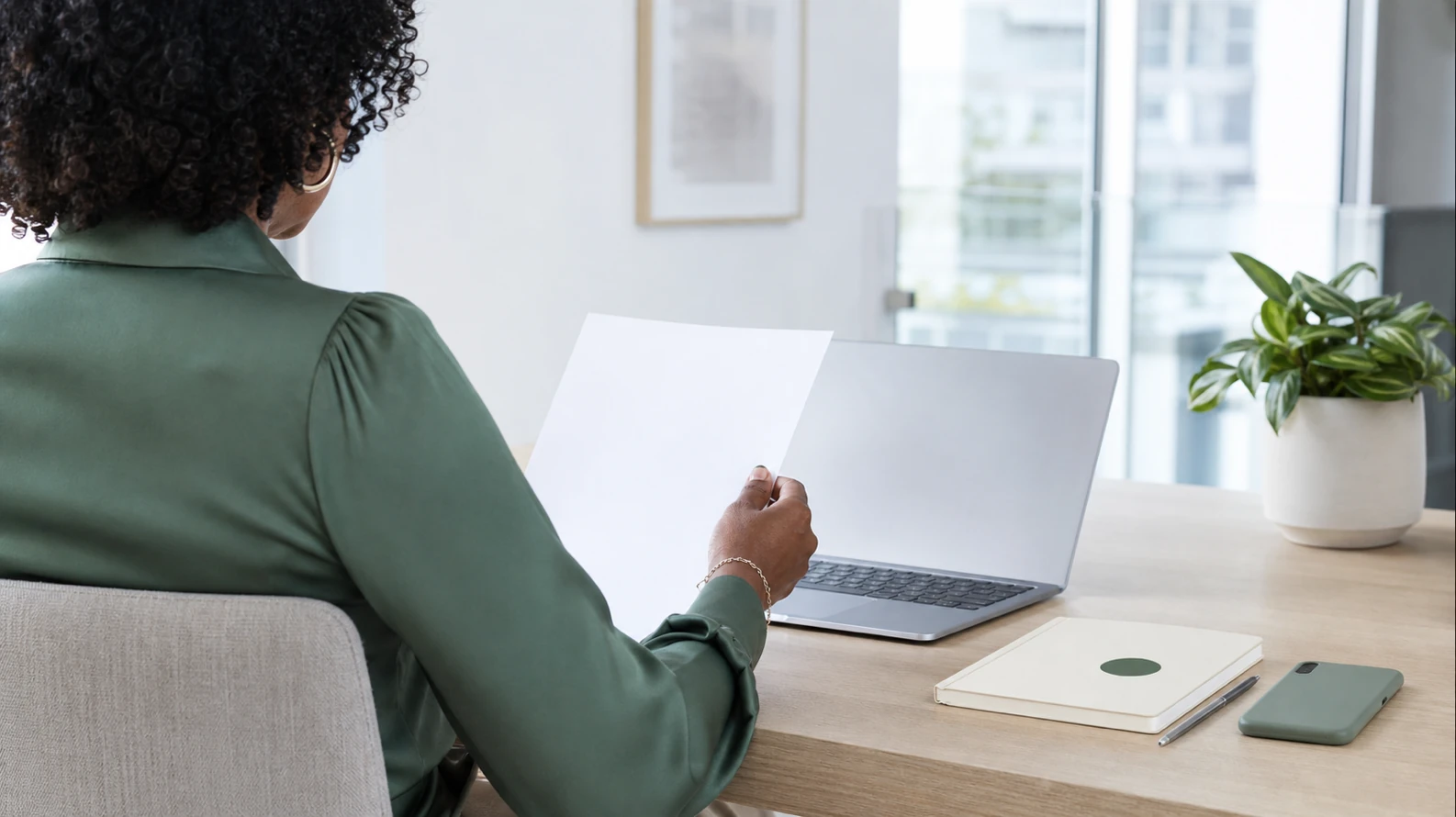 A person at a desk in warm evening light, reviewing a printed job-offer letter next to an open laptop, calm and considering rather than anxious